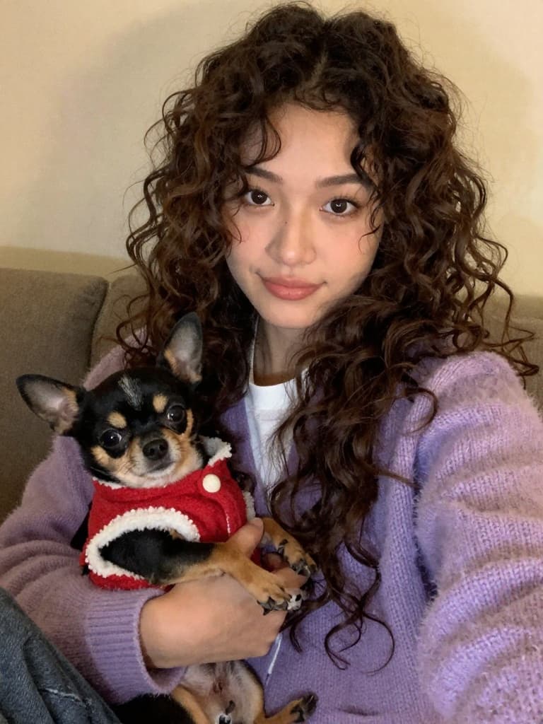 Front-facing camera selfie of a young mixed-race woman with long…