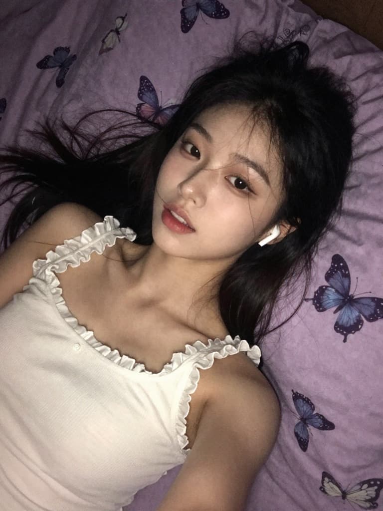 Smartphone selfie of a beautiful young East Asian woman lying on her…