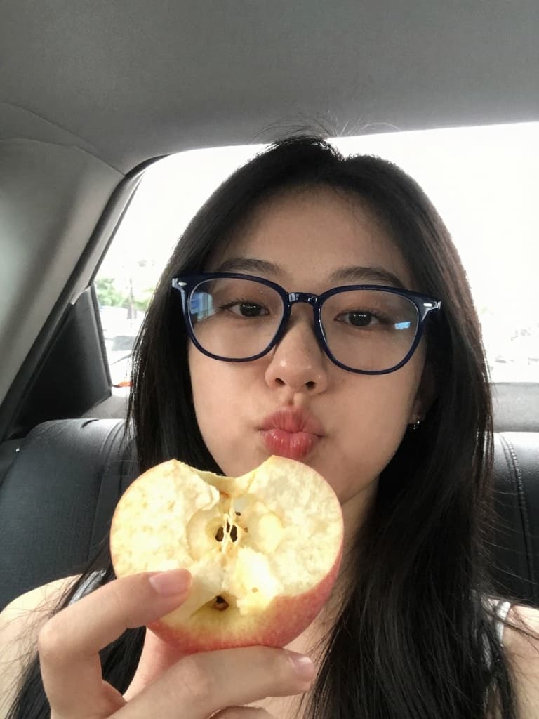 Smartphone selfie of a young East Asian woman inside a car, holding a…